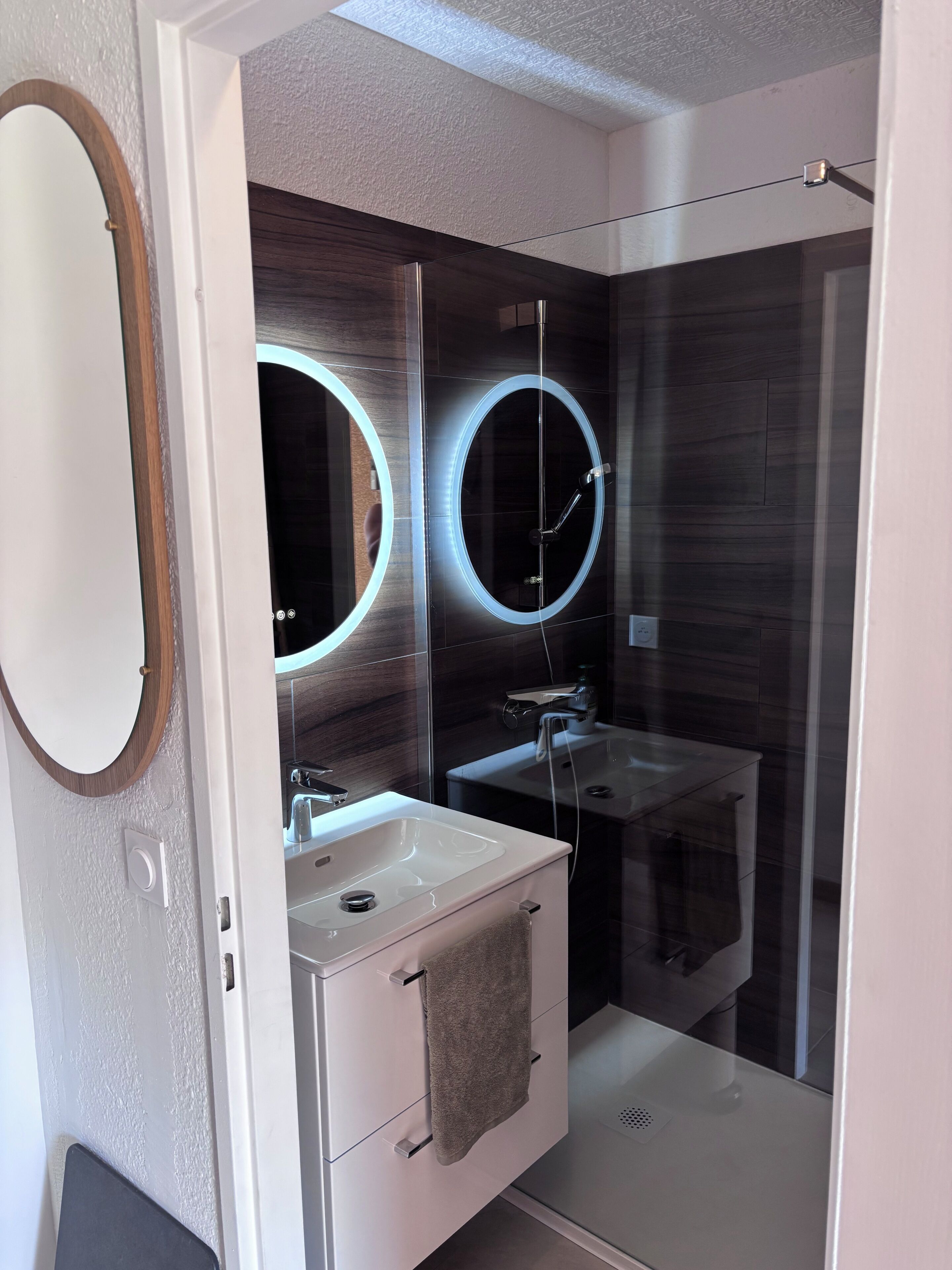 Ein modernes Badezimmer mit Duschkabine aus Glas, einem Waschtisch mit Spiegel und einem Handtuchhalter.