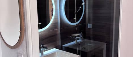 A modern bathroom with a glass shower enclosure, a vanity with a mirror, and a towel rack.