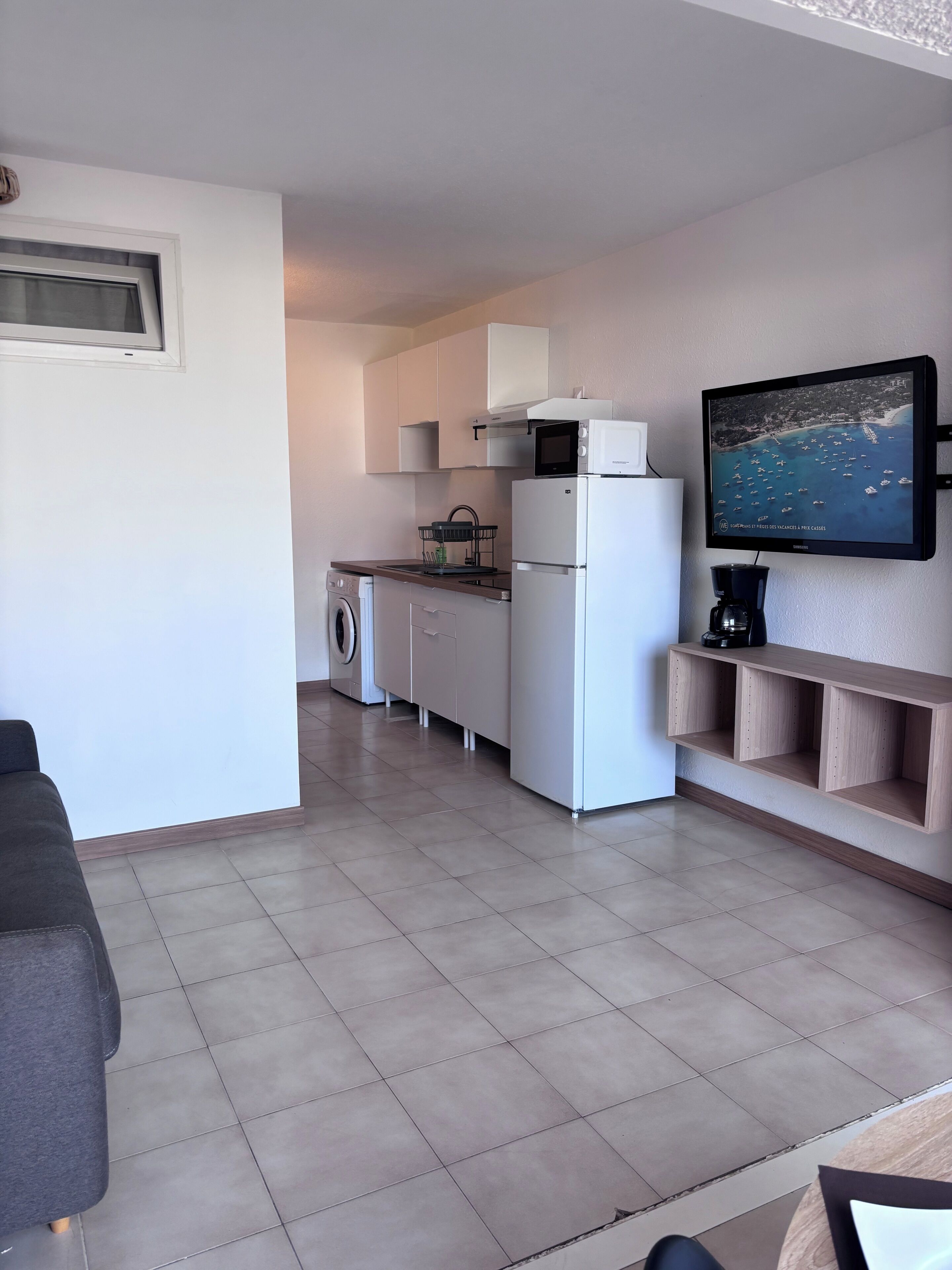 A compact living space with a kitchenette, a washing machine, a flat-screen TV, and a coffee maker.