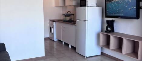 A compact living space with a kitchenette, a washing machine, a flat-screen TV, and a coffee maker.