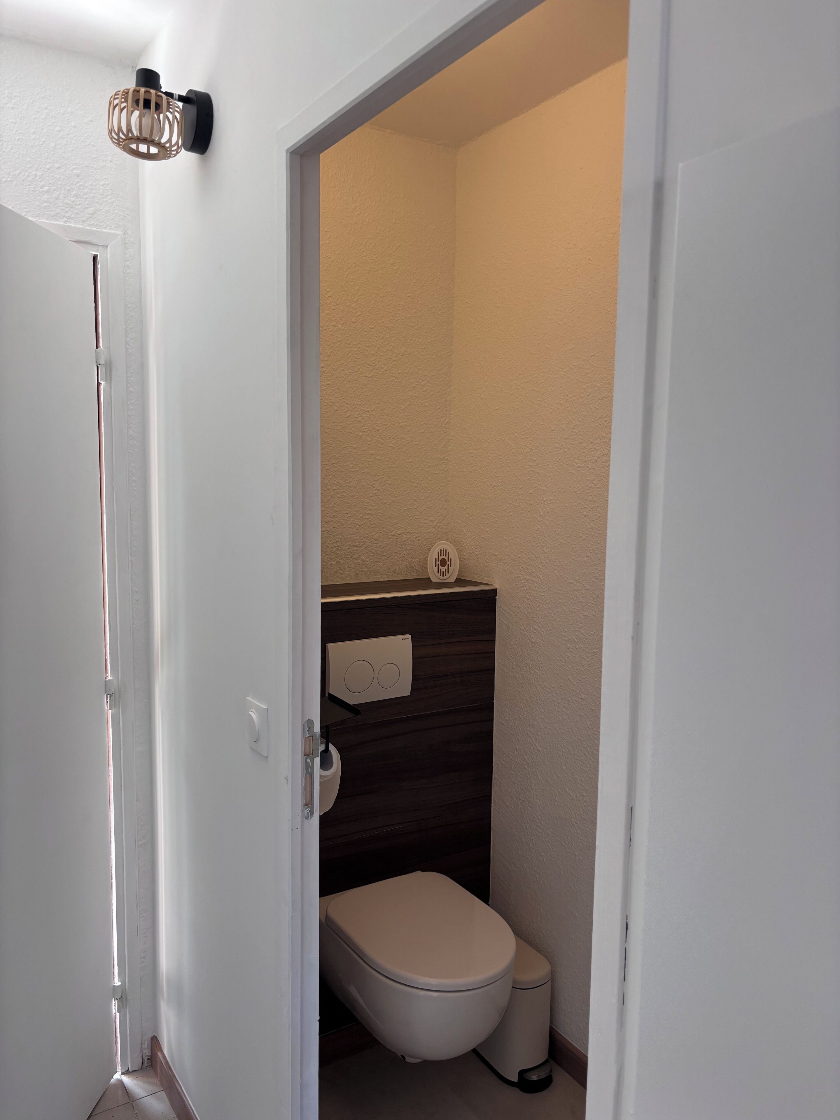 Et lille, smalt badeværelse med toilet, håndklædeholder og vægmonteret lysarmatur.