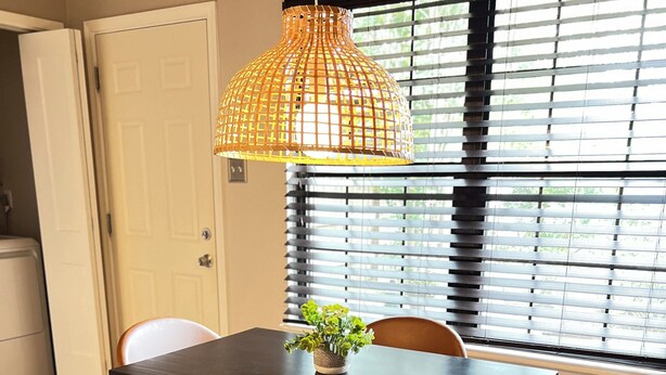 A dining area with a table and chairs, a hanging light fixture, and a window with blinds. - Rest Haven - Cozy, 2 bedroom Townhome (Spring)