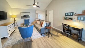 A modern living room with a blue armchair, a sofa, a coffee table, and a ceiling fan. - Rest Haven - Cozy, 2 bedroom Townhome (Spring)