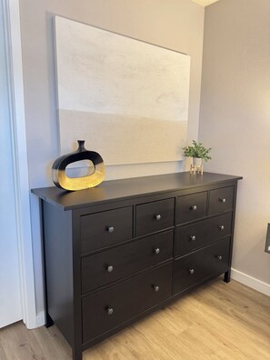 A dark wooden dresser with multiple drawers, a round metallic object on top, and a small potted plant beside it. - Rest Haven - Cozy, 2 bedroom Townhome (Spring)