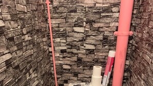 A bathroom with a stone wall, a toilet labeled 'THE THRONE,' a pink pipe, and a black rug.
