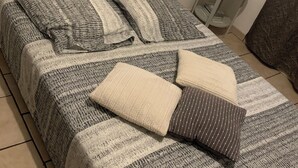 A bed with a striped bedspread and two pillows, a small bedside table with a lamp, and a patterned curtain partially visible.