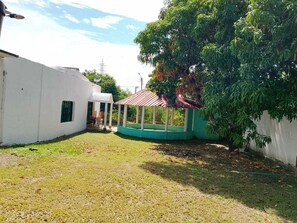 A courtyard with a covered seating area, a white building, and a tree.