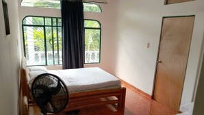 A small, single-room accommodation with a bed, a standing fan, and a door. - Girardot Vacation Rental: Your Relaxation Guaranteed (Cundinamarca)
