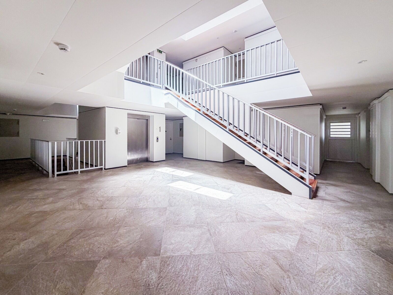 A spacious interior with a central staircase, multiple doors, and a high ceiling.