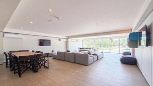 Ein modernes Wohnzimmer mit Essbereich, großen Fenstern und einem an der Wand befestigten Flachbildfernseher.