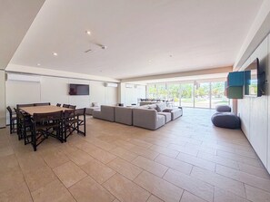 A modern living room with a dining area, large windows, and a flat-screen TV mounted on the wall. - Sophisticated Maho Studio with Resort-Style Amenities in a Gated Community. (Maho)