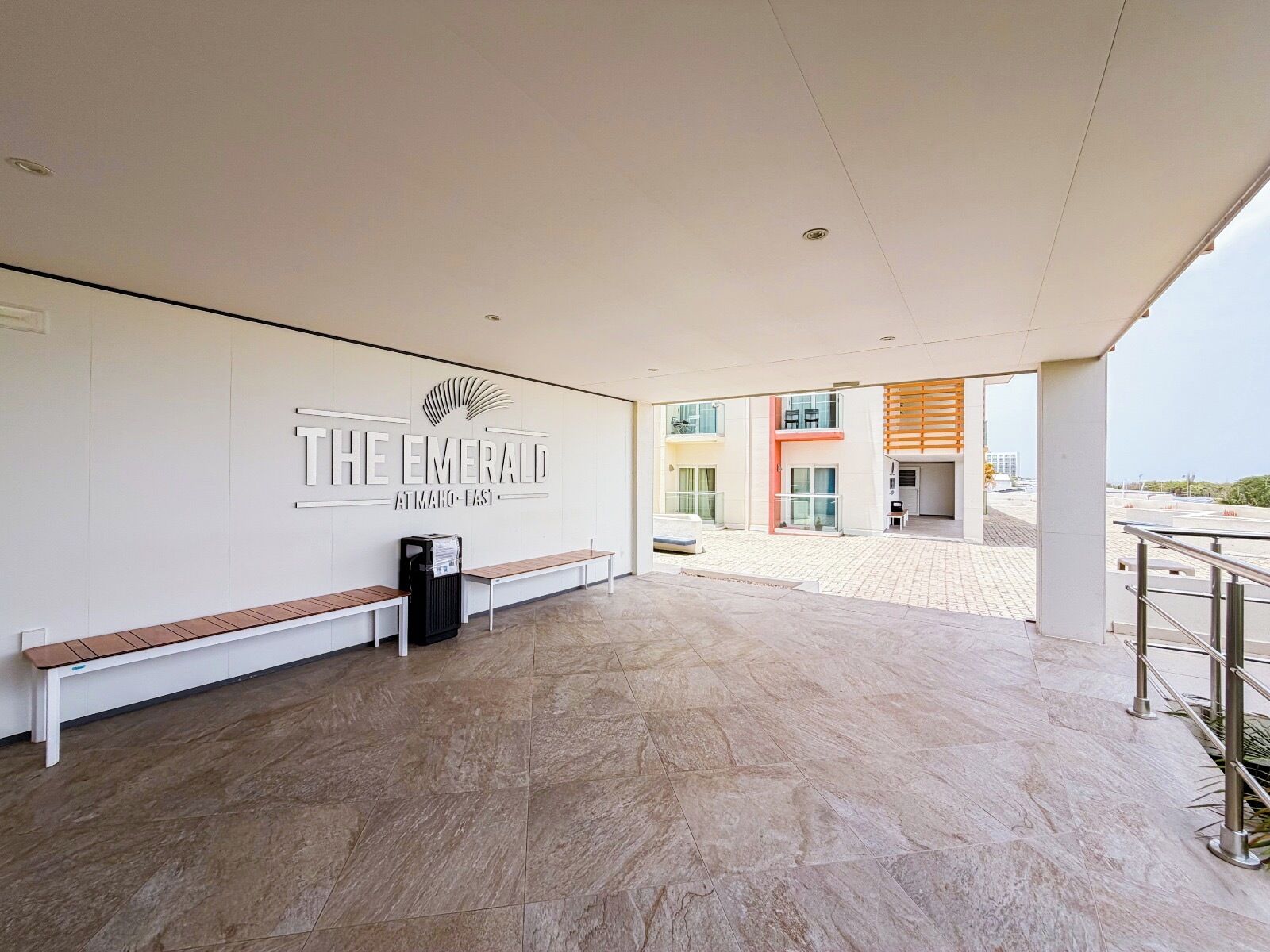 A reception area with a bench, a trash bin, and a wall with the hotel's name.