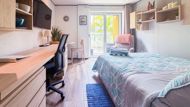 Ein modernes Schlafzimmer mit Schreibtisch, Stuhl, Bett und Blick ins Freie.