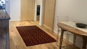A hallway with wooden flooring, a red patterned rug, a dining table with chairs, and wooden doors. - Le Bi-Fûts - ALLEVARD (ALLEVARD)