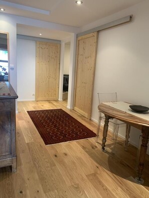 Ein Flur mit Holzboden, einem roten Teppich mit Muster, einem Esstisch mit Stühlen und Holztüren.