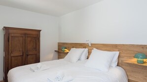 A bedroom with a wooden wardrobe, a bed with white bedding, and a bedside table with a lamp. - Le Bi-Fûts - ALLEVARD (ALLEVARD)