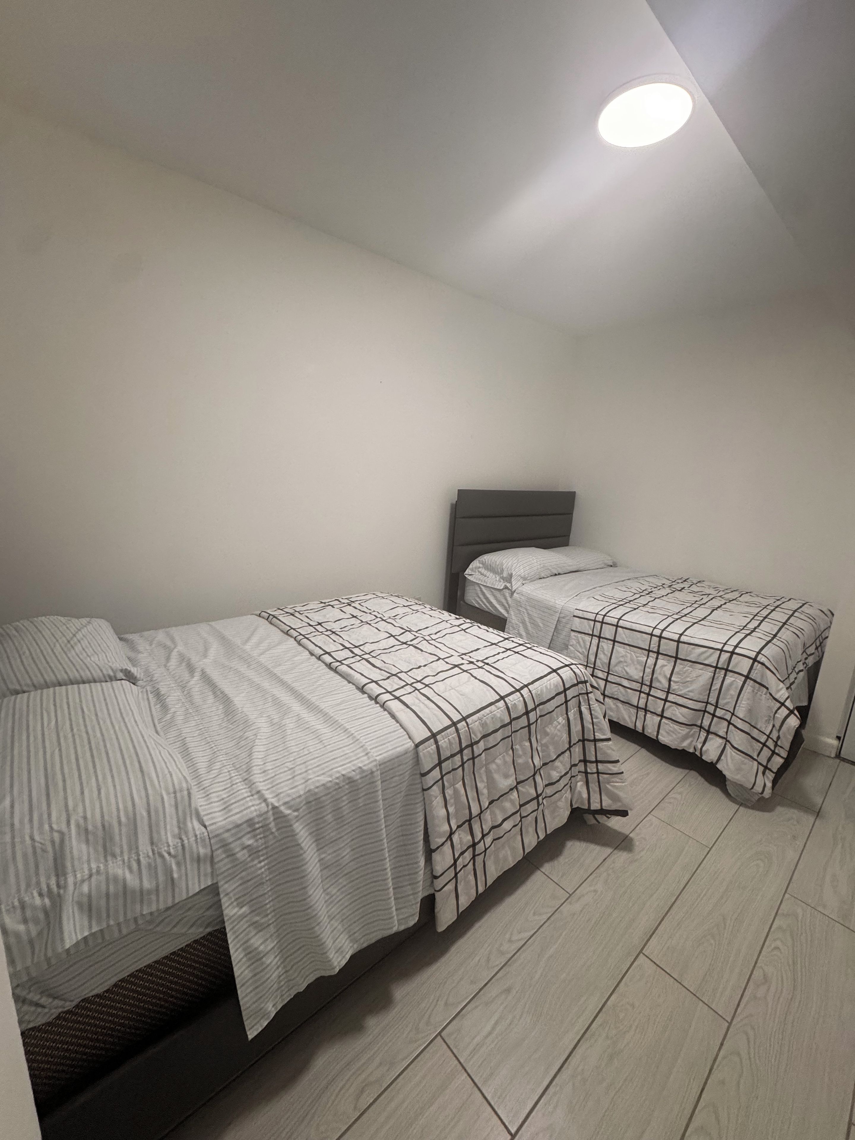 Una habitación con dos camas, cada una con una colcha de diseño diferente, una lámpara de techo sencilla y suelo de madera.