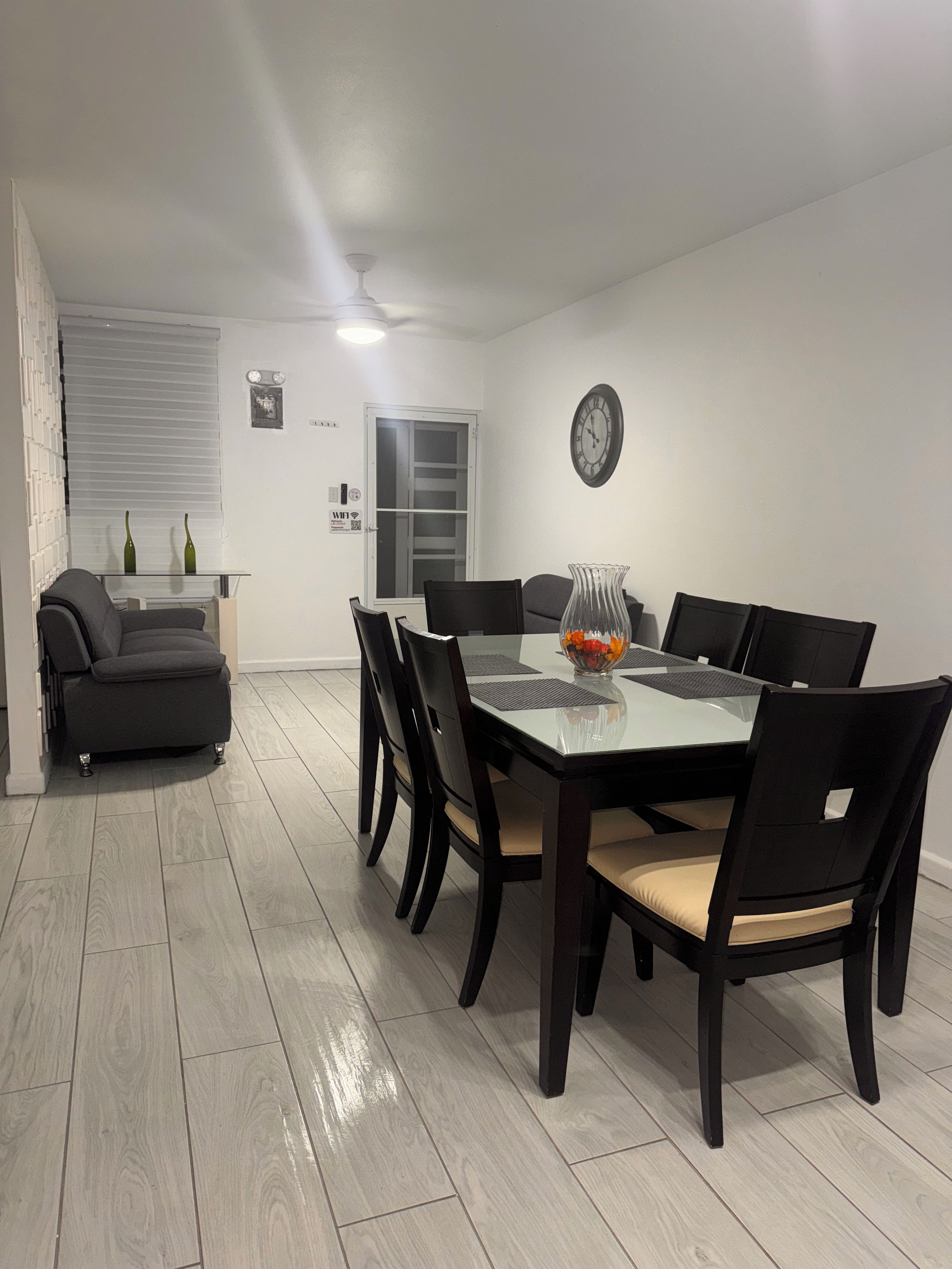 Un comedor con una mesa de vidrio, sillas negras y un florero con flores.