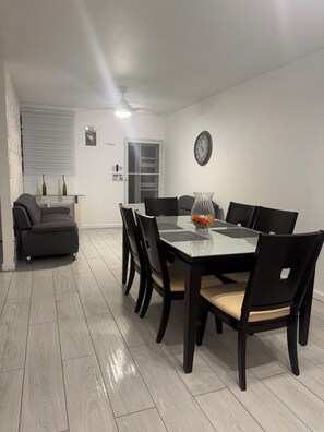 A dining area with a glass-top table, black chairs, and a vase with flowers. - Casa Patriota (Lares)