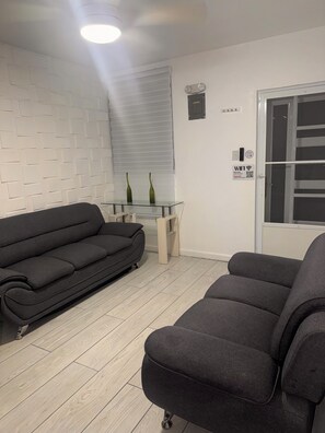 A modern living room with a grey sofa, a glass coffee table, and a white brick wall. - Casa Patriota (Lares)