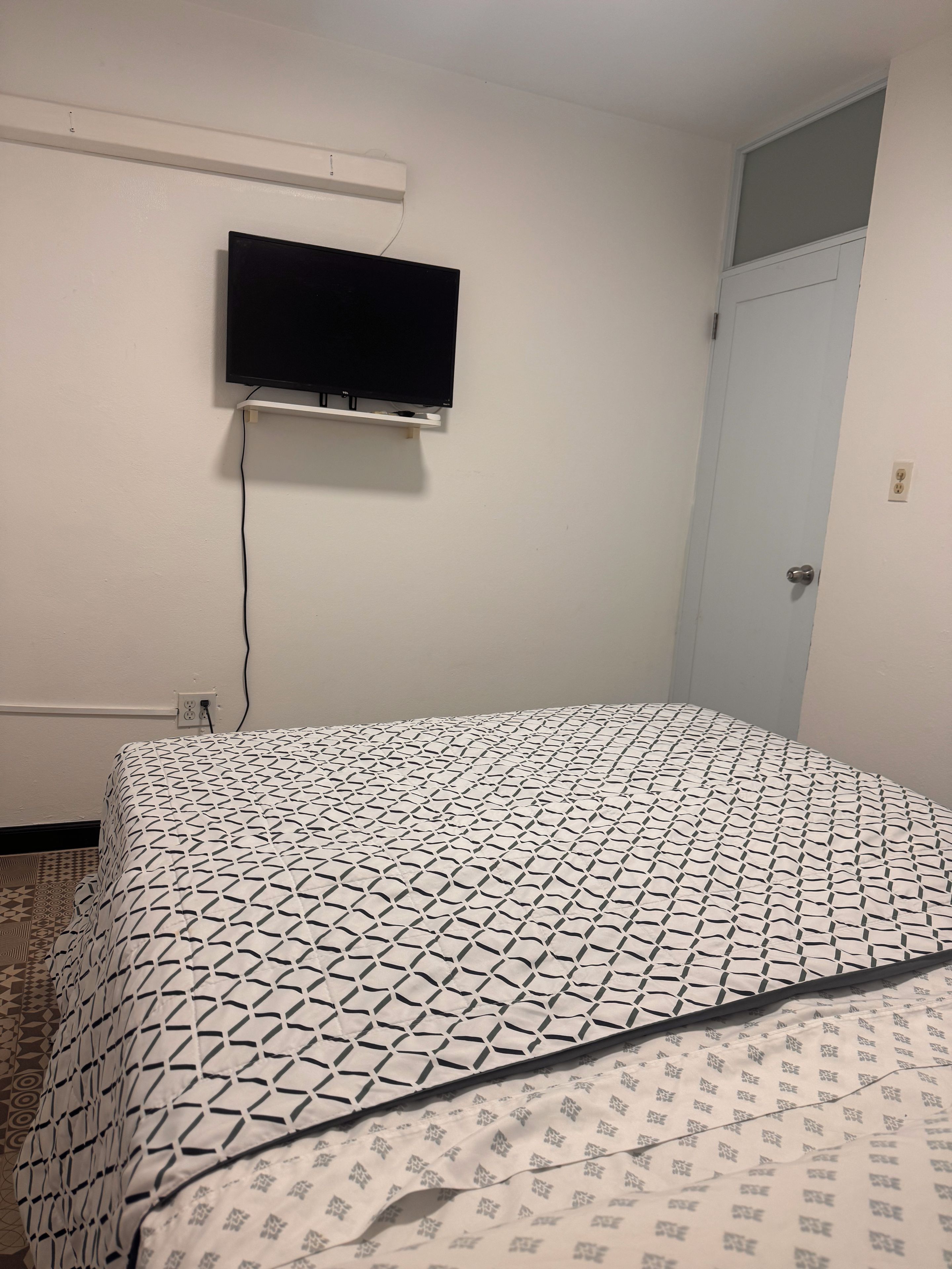 Ein Schlafzimmer mit einem Bett, einem an der Wand befestigten Fernseher und einer Tür.