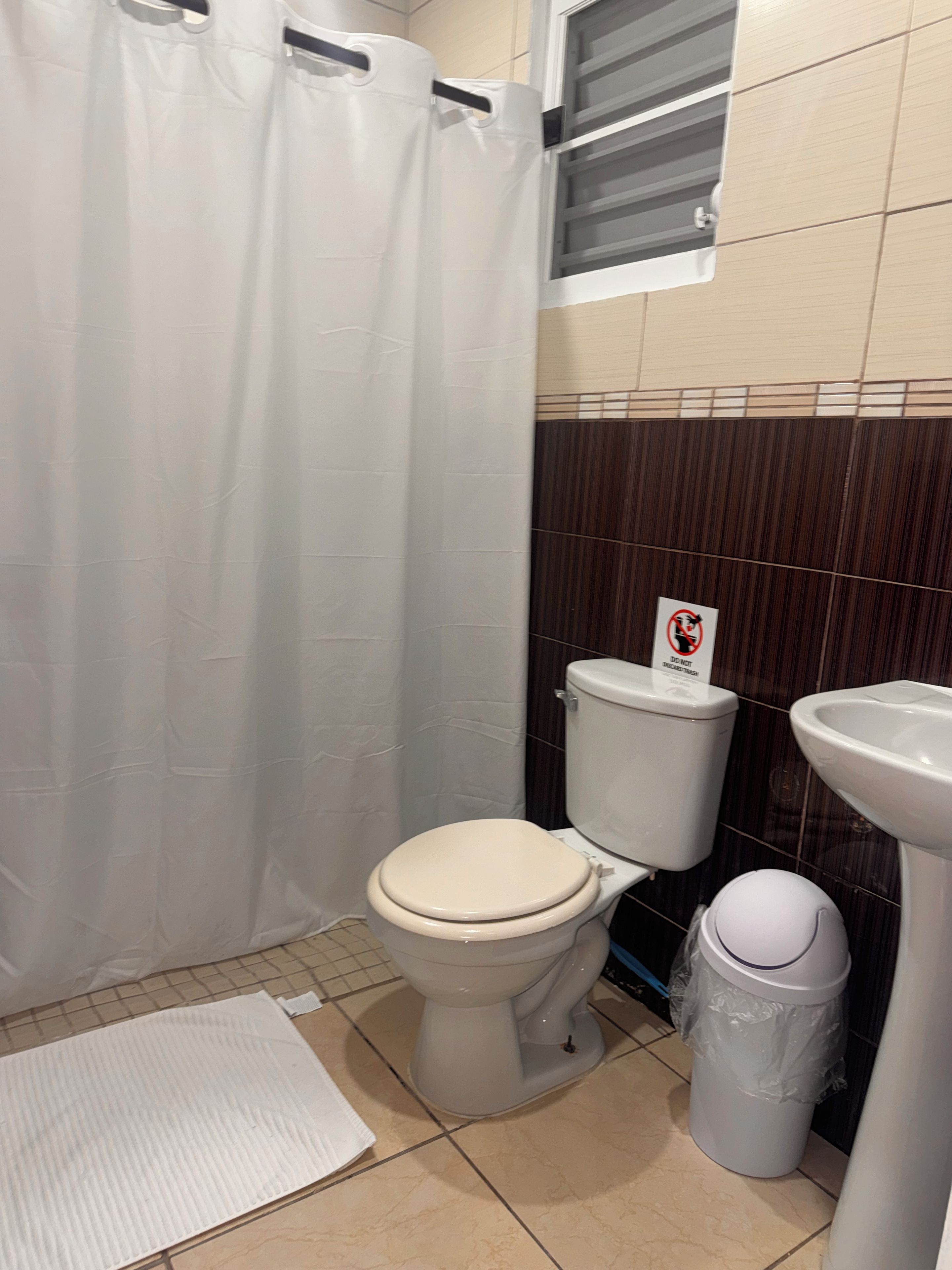 Un baño con inodoro, lavamanos, cubo de basura y cortina de ducha.