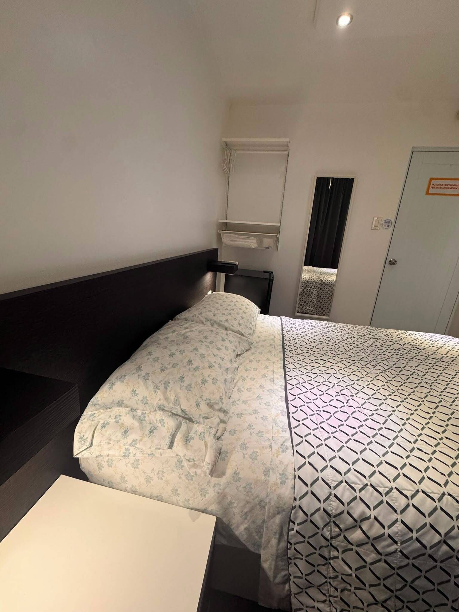 A hotel room with a bed, a bedside table, a mirror, and a door.