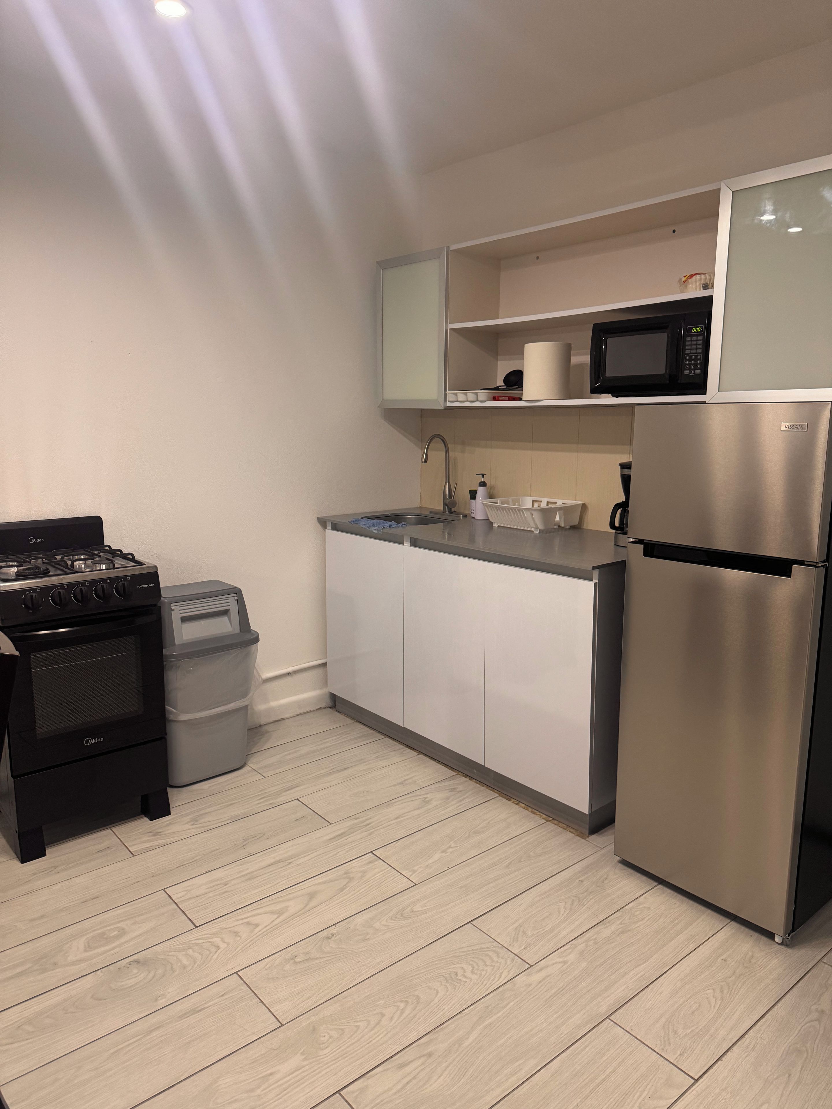 A compact kitchen with a stainless steel refrigerator, a microwave, a gas stove, and a sink.