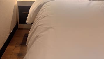 A neatly made bed with white linens, a bedside table with a lamp, and a framed picture on the wall.
