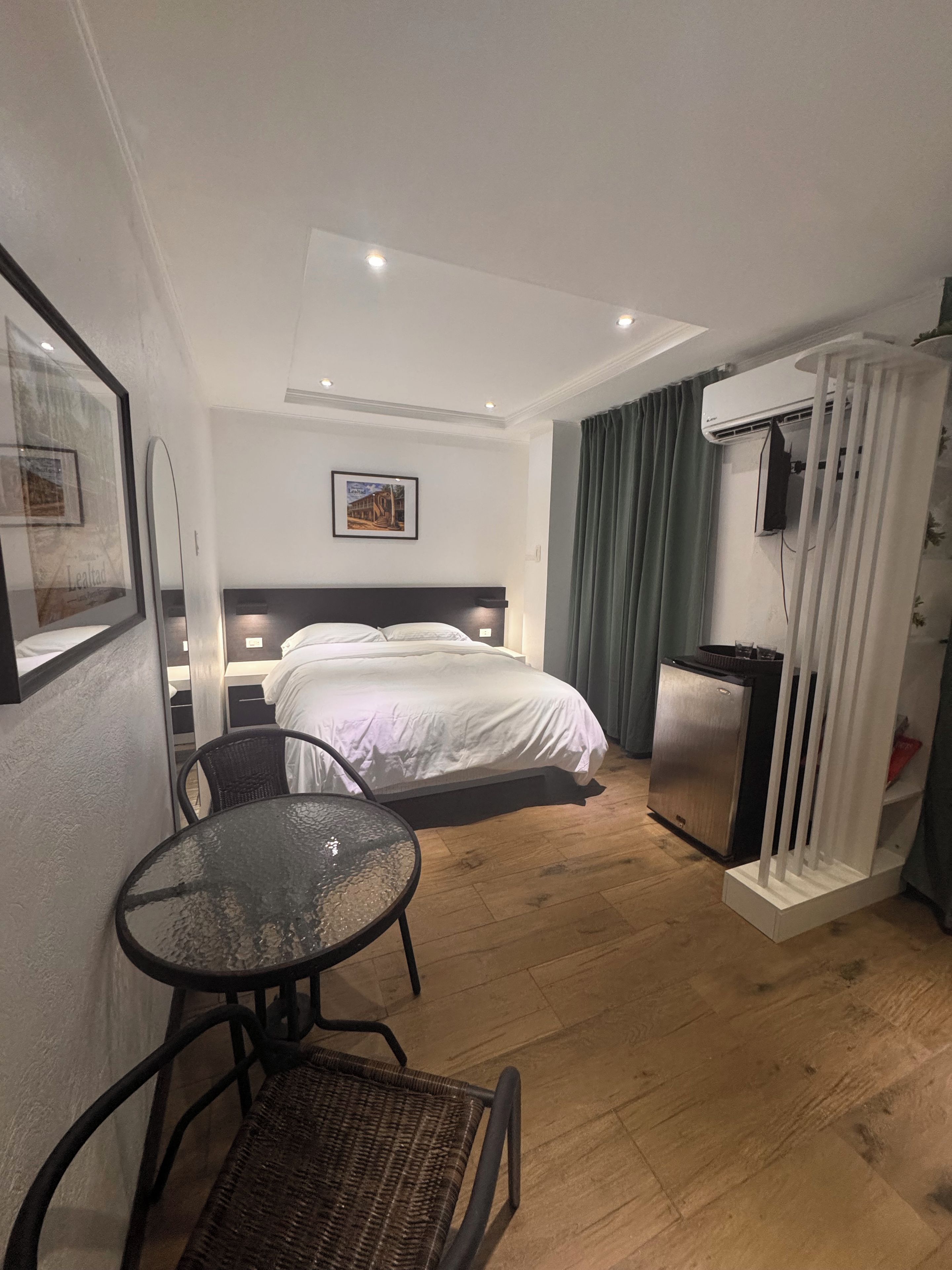 Habitación de hotel con cama, una mesita, una silla, refrigerador y aire acondicionado.