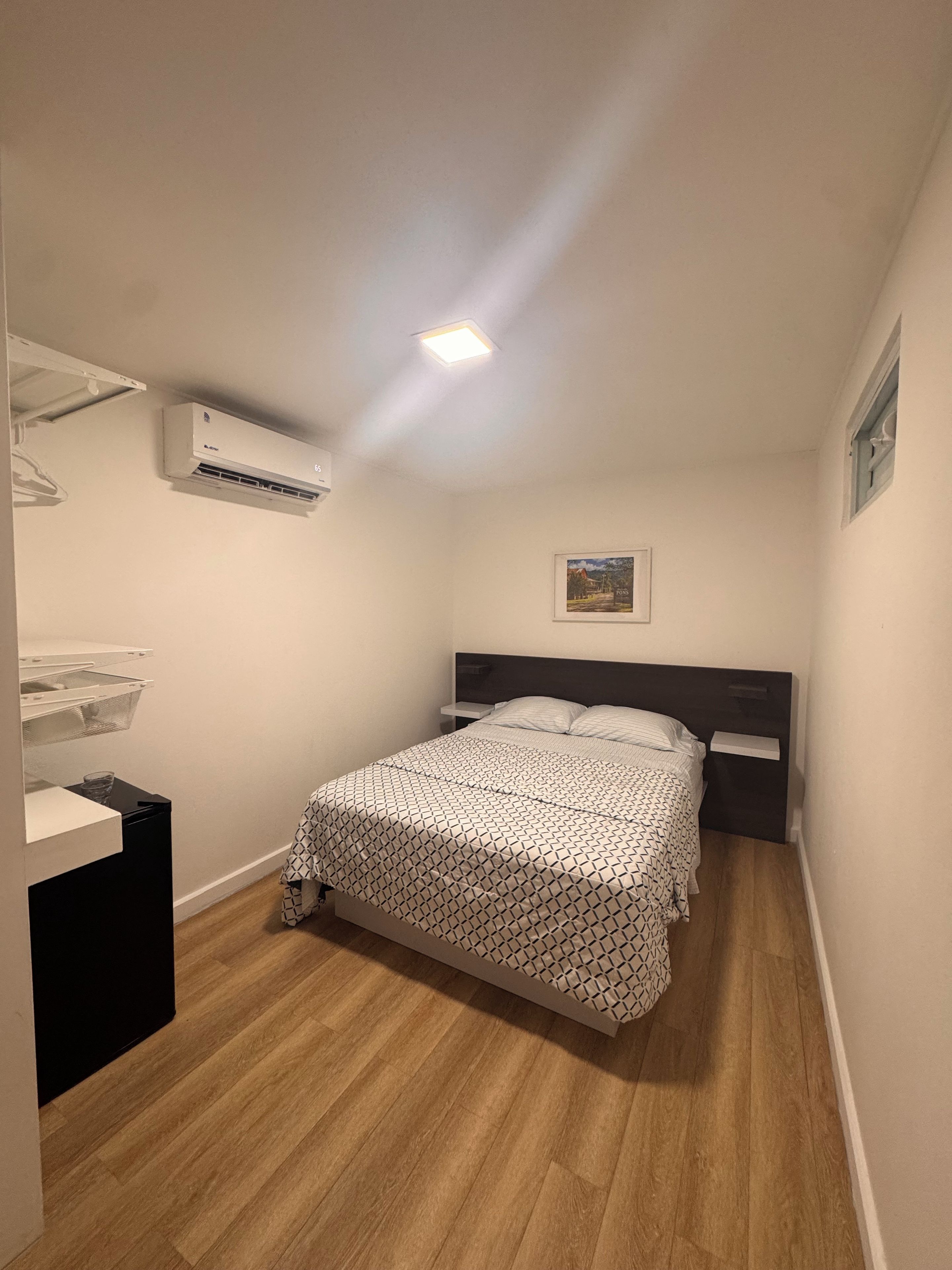 Een slaapkamer met een bed, nachtkastjes, een airconditioning en een ingelijste foto aan de muur.