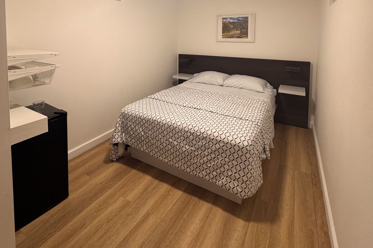 A bedroom with a bed, bedside tables, an air conditioning unit, and a framed picture on the wall.