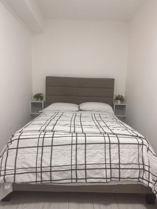 A bed with a headboard, a white and black checkered bedspread, and two bedside tables with plants. - Casa Patriota (Lares)