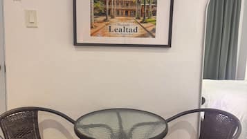 A framed picture of a building with the text 'Hacienda Lealtad Lares, Puerto Rico' on a wall. There is a round glass table with two wicker chairs in front of it.