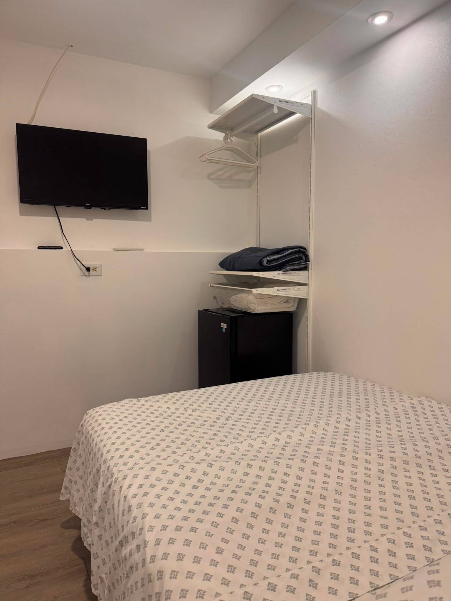 A bedroom with a bed, a TV mounted on the wall, a small desk with a mirror, and a wardrobe.