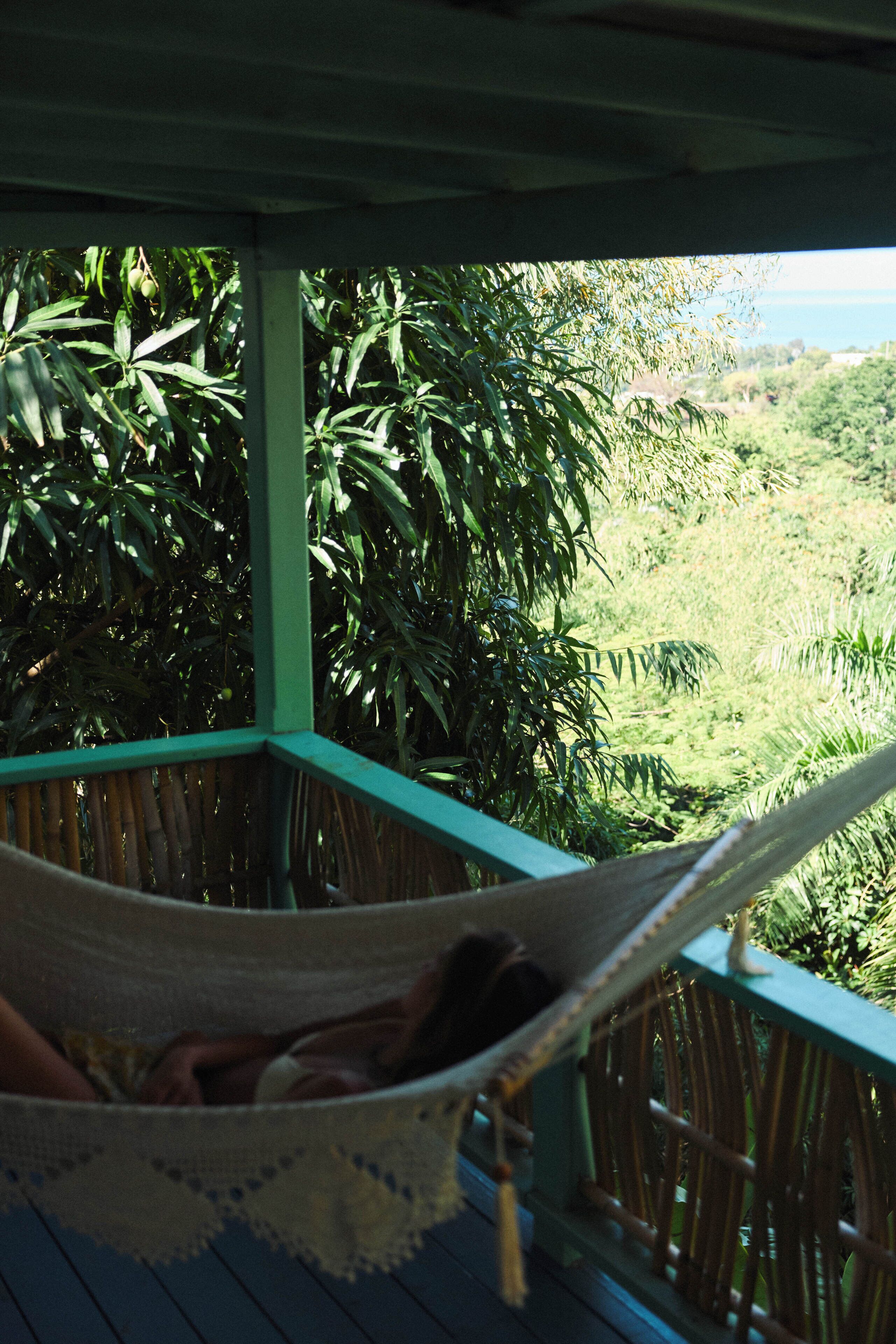 A hammock on a wooden deck with a view of a lush green landscape.