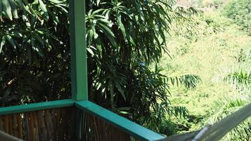 A hammock on a wooden deck with a view of a lush green landscape.