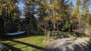 A hammock in a wooded area with a gravel path and a wooden fence. - Quiet and Private Tiny Home with Outdoor Bath in Hanmer Springs (Hanmer Springs)
