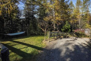 A hammock in a wooded area with a gravel path and a wooden fence.