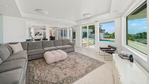 Ein geräumiges Wohnzimmer mit einem grauen Ecksofa, einem großen Teppich und Blick auf einen Swimmingpool und eine Außenanlage.