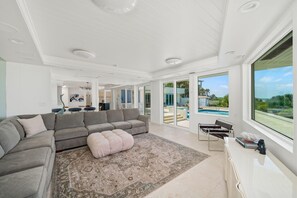 A spacious living room with a grey sectional sofa, a large rug, and a view of a swimming pool and outdoor area. - Panoramic Paradise I Luxury Beachfront Estate & Boardwalk to the Beach (Saint Augustine)