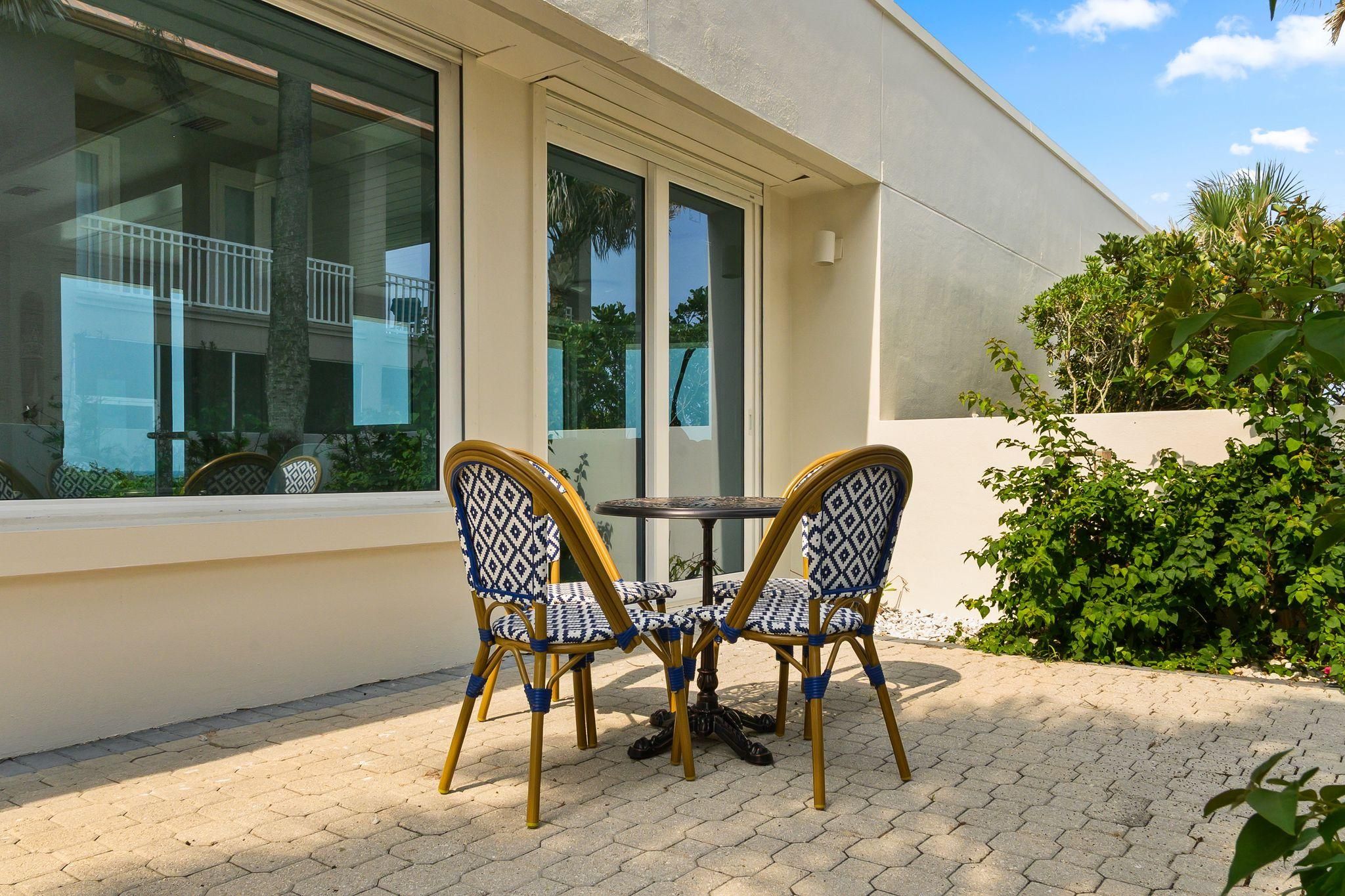 Un espace extérieur aménagé avec une table et quatre chaises, une fenêtre donnant sur un bâtiment et une plante en pot.