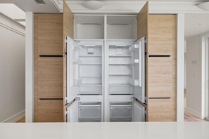 A modern kitchen with a built-in double-door refrigerator, wooden cabinetry, and a white countertop. - Panoramic Paradise I Luxury Beachfront Estate & Boardwalk to the Beach (Saint Augustine)