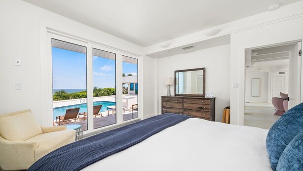 Ein Schlafzimmer mit einem großen Bett, einem Schminktisch und Blick auf Pool und Außenbereich.