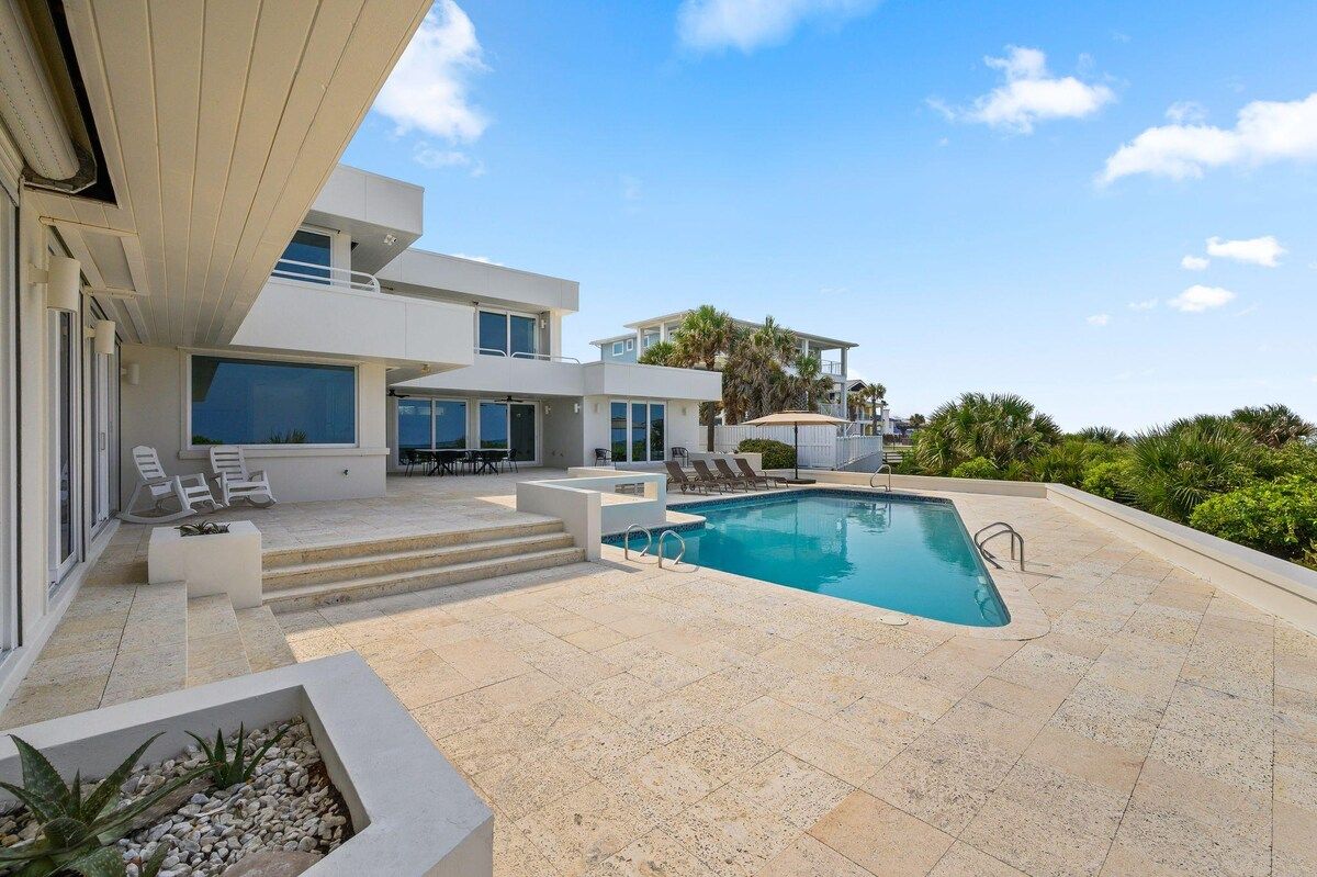 A modern poolside area with a clear blue pool, lounge chairs, and a two-story building with large windows.