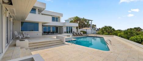 A modern poolside area with a clear blue pool, lounge chairs, and a two-story building with large windows.