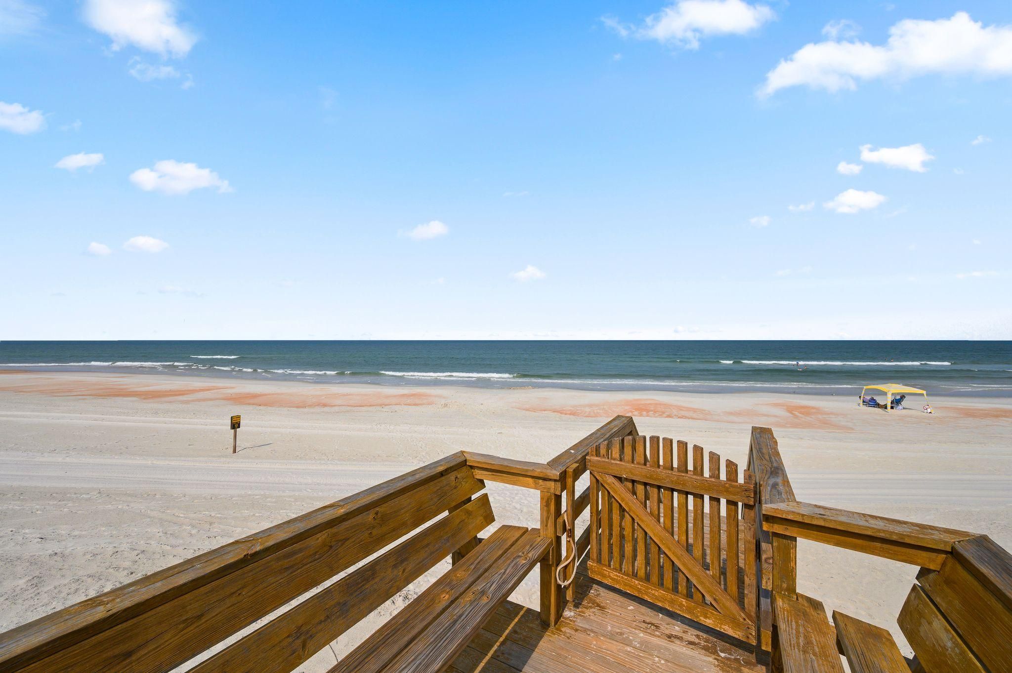 A wooden boardwalk leading to a beach with a clear sky and ocean view.