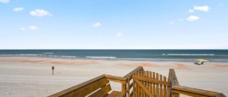 A wooden boardwalk leading to a beach with a clear sky and ocean view.