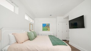 Ein Schlafzimmer mit einem Bett, einem Bild, einem Fernseher und einer Tür.