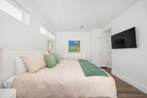 A bedroom with a bed, a painting, a television, and a door. - Panoramic Paradise I Luxury Beachfront Estate & Boardwalk to the Beach (Saint Augustine)